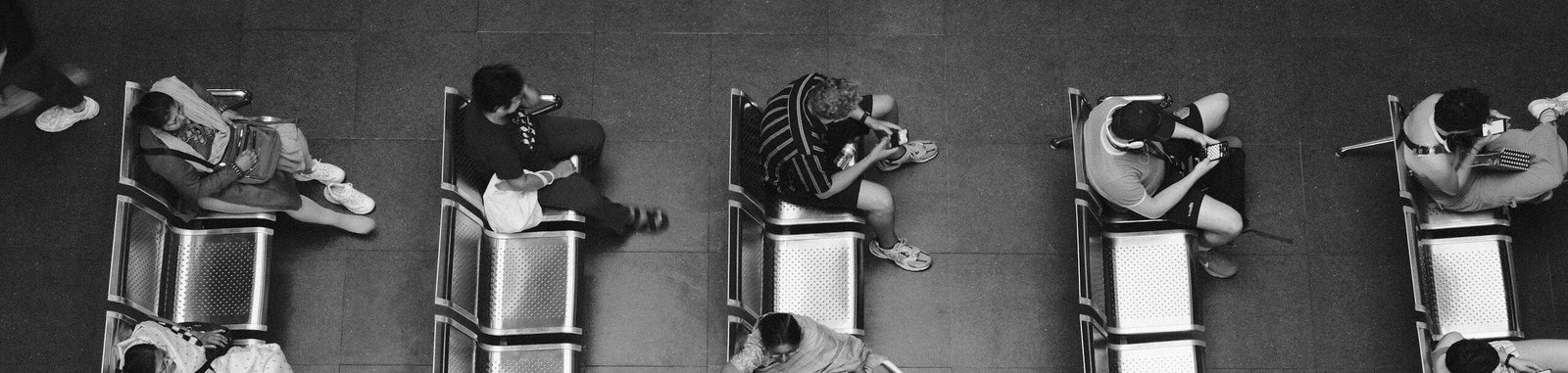 Black and white high angle photo of people sitting and waiting at a station.