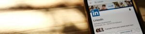 Close-up of a smartphone showing a LinkedIn profile page on a wooden table with shadows.