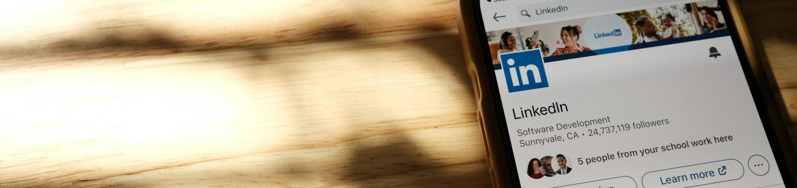 Close-up of a smartphone showing a LinkedIn profile page on a wooden table with shadows.