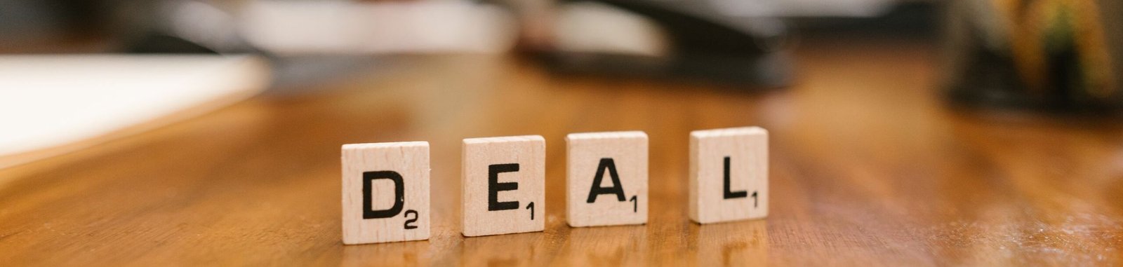 Close-up of Scrabble tiles spelling 'deal' with a handshake in the background.