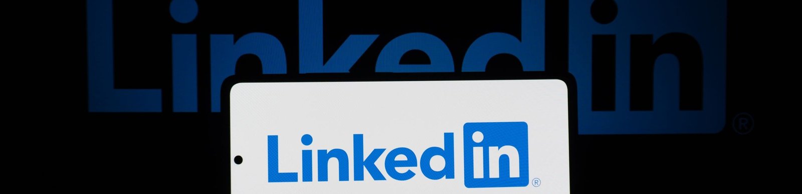 Smartphone showing LinkedIn logo with keyboard and large background logo, business theme.